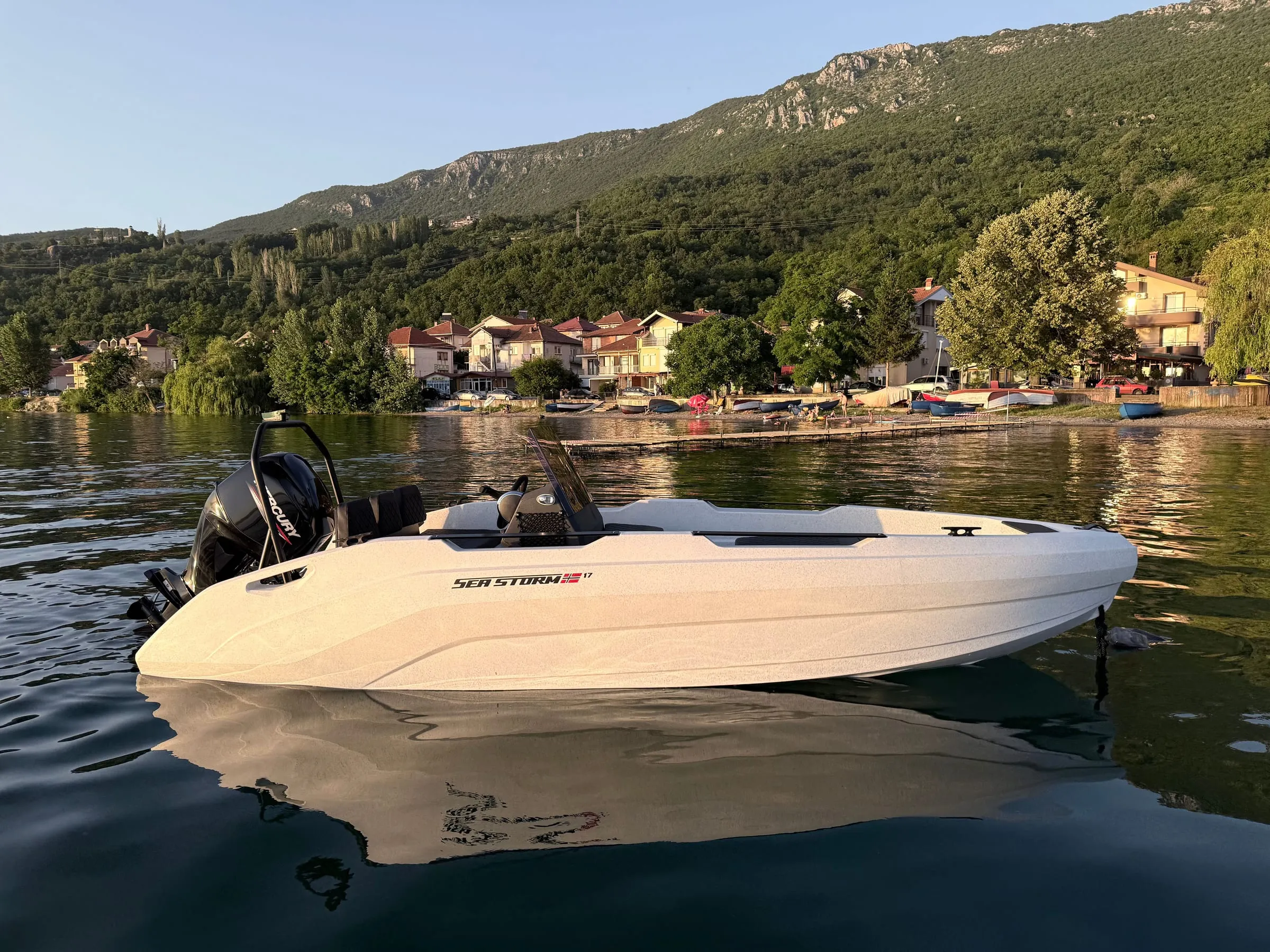 SeaStorm 17 in evening light in front of a lakeside mountain village, ready for rental and charter